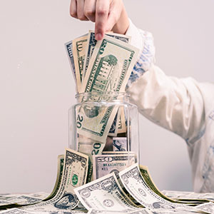 Hand placing dollar bills into a glass jar, symbolizing saving or managing money.