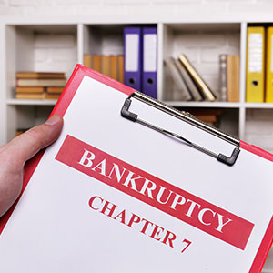 Hand holding red clipboard with 'BANKRUPTCY CHAPTER 7' document.