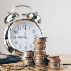 Stacked coins and an alarm clock on a table, symbolizing Creditor Harassment and Abuse.
