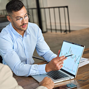 Financial advisor points to a laptop screen displaying a graph, explaining data to a client.
