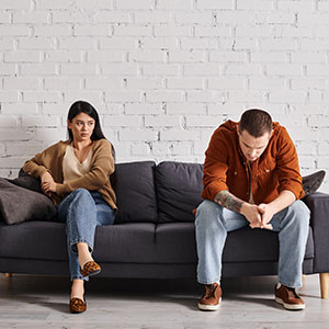 A man and a woman sit on opposite sides of a couch, looking distressed, symbolizing a marital dispute or separation.