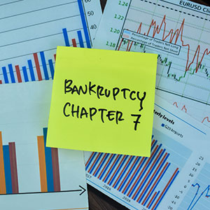 A yellow sticky note with 'BANKRUPTCY CHAPTER 7' on financial charts.