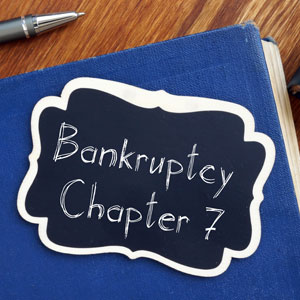 A close-up of a blue book with a black label that says 'Bankruptcy Chapter 7' in white chalk writing.