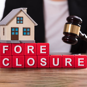 A house model and a gavel are placed on red blocks spelling 'FORECLOSURE,' symbolizing legal action against a home.
