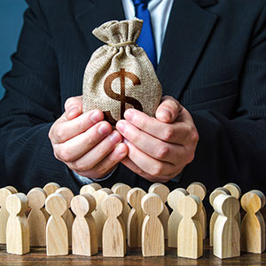 Business person holds a money bag with a dollar sign over wooden figures, symbolizing financial distribution.