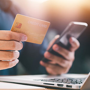 Person holds credit card, using a smartphone and laptop, for credit card management.