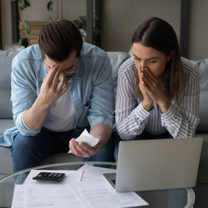 Worried couple reviews financial documents and laptop, potentially facing bankruptcy.