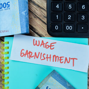 Note with 'WAGE GARNISHMENT' and cash, next to a calculator and notebook.