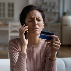 Woman looking distressed while on the phone and holding a credit card, indicating debt collector interaction.