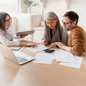 Financial advisor assists a couple with documents and a calculator, likely related to financial planning or debt management.