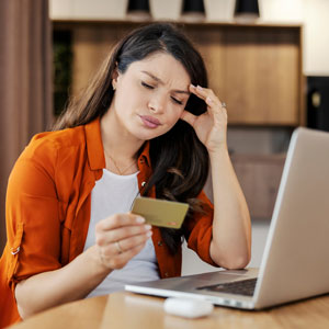 Stressed woman holding a credit card while looking at a laptop, illustrating creditor harassment.