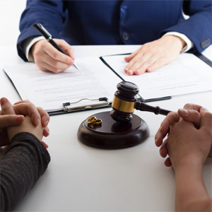 Two individuals, a lawyer, a gavel, and wedding rings on a table, symbolizing bankruptcy considerations for couples.